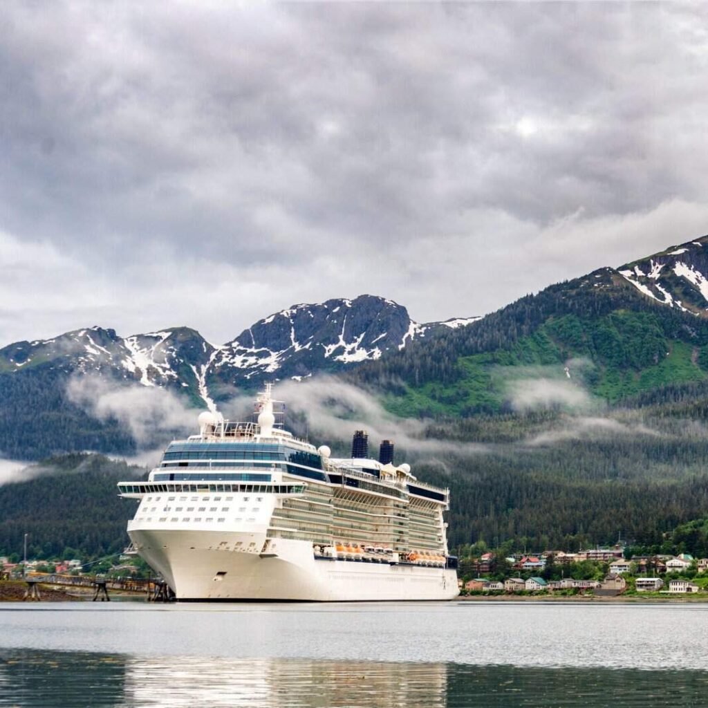 Large cruise ship sailing in Alaska with snow-capped mountains and lush green forests.