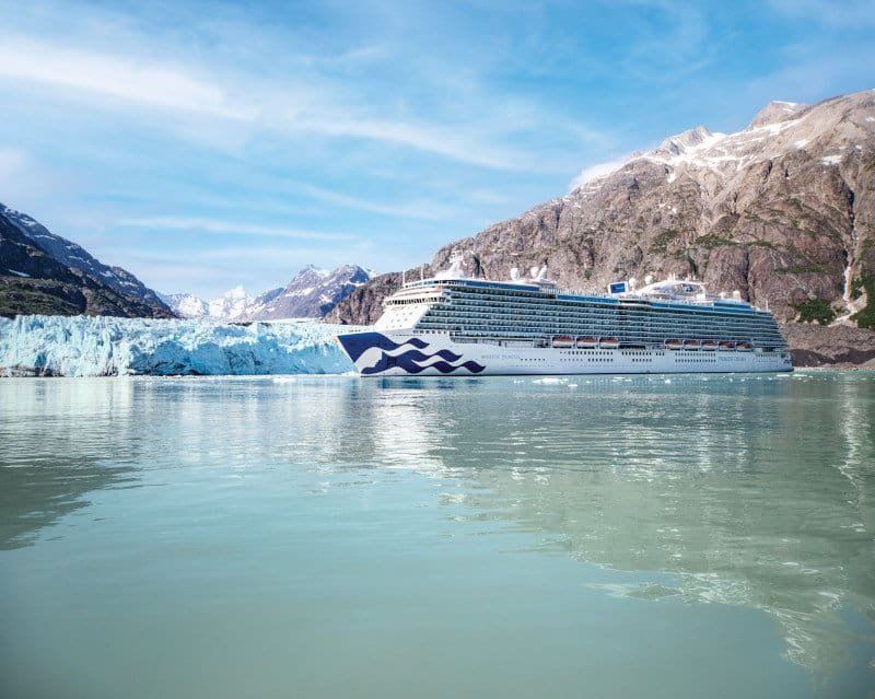 Large cruise ship sailing through Glacier Bay surrounded by snow-capped mountains.