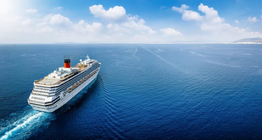 Large cruise ship sailing on calm blue ocean under clear sky.