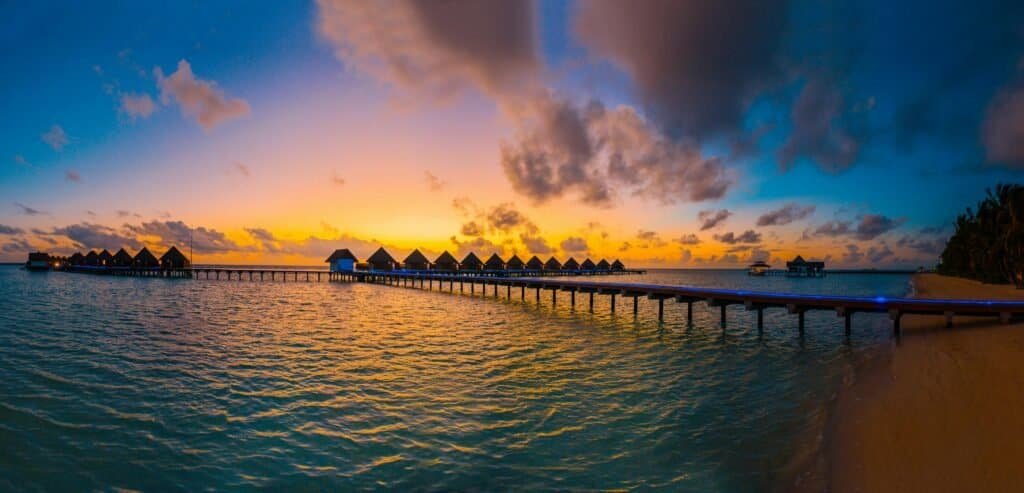 Overwater bungalows at sunset with vibrant sky and calm turquoise waters, perfect for luxury travel.