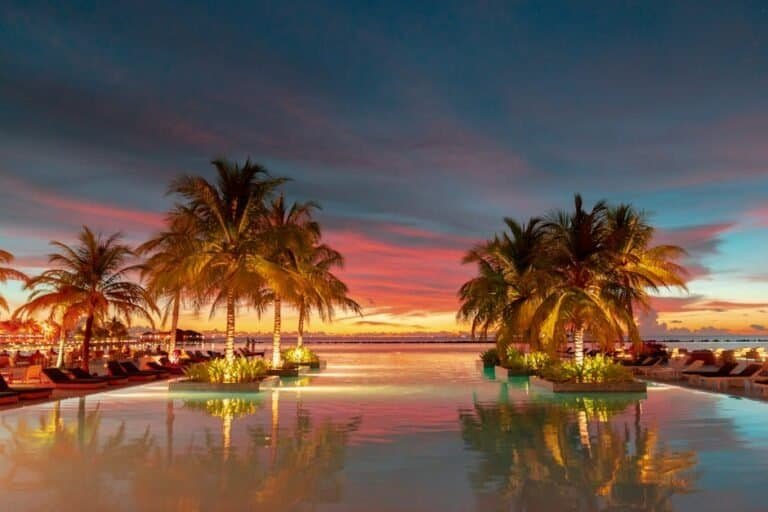Sunset over tropical pool with palm trees and lounge chairs at a luxury resort.