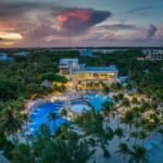 Beautiful tropical beach resort with pool and palm trees at sunset.