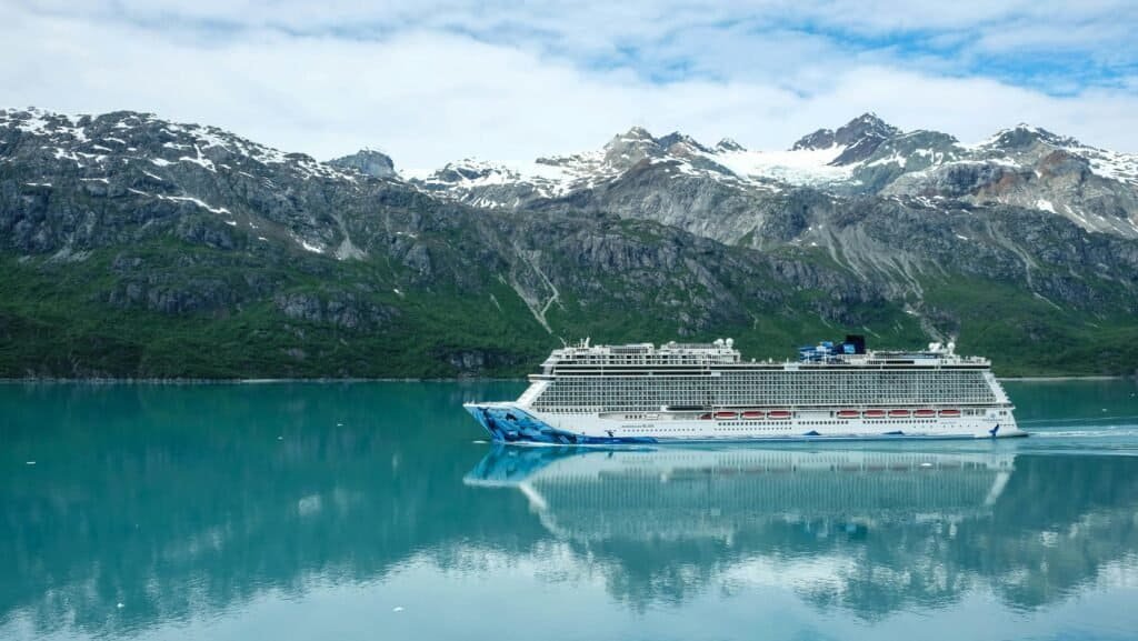 Large cruise ship sailing through Glacier Bay with snow-capped mountains in the background.