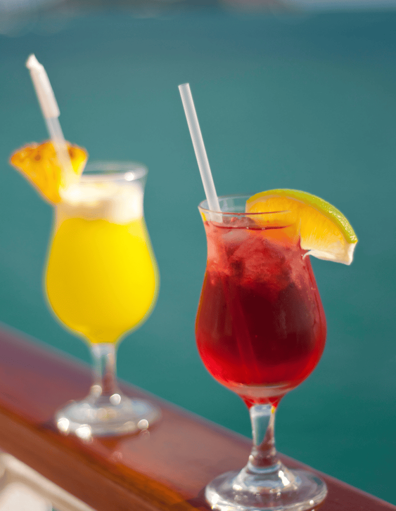 Colorful tropical cocktails with fruit garnishes on a poolside table.