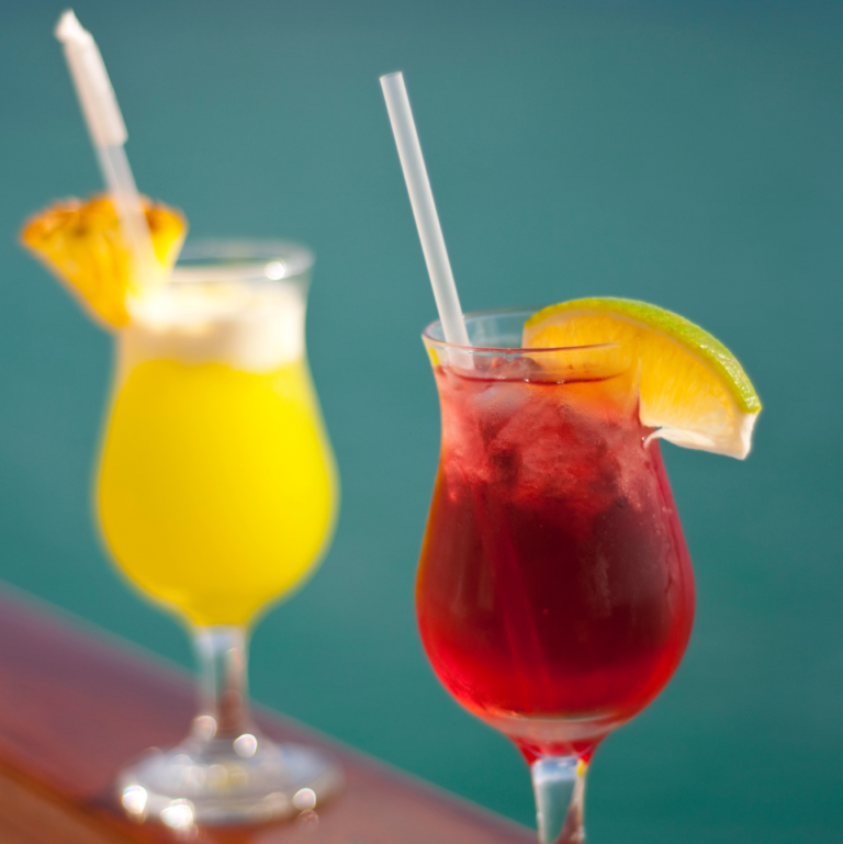 Colorful tropical cocktails with fruit garnishes on a poolside table.