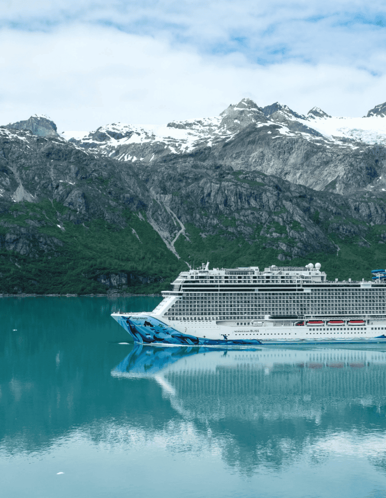 Cruise ship sailing in Alaska with snow-capped mountains in background.