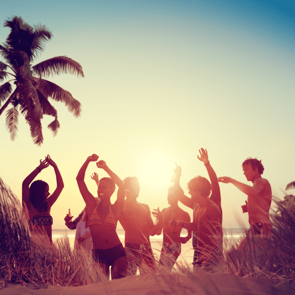 Group of friends dancing and enjoying sunset on the beach with palm trees.