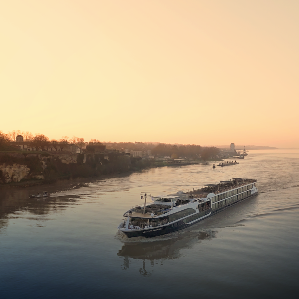 Passenger boat sailing on calm river during sunset with shoreline in background.