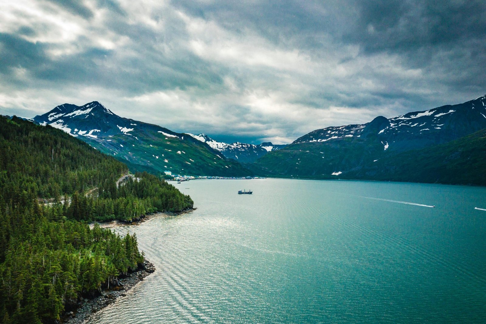 Majestic aerial view of an Alaskan fjord, with snow-capped mountains and turquoise waters creating a dramatic landscape.